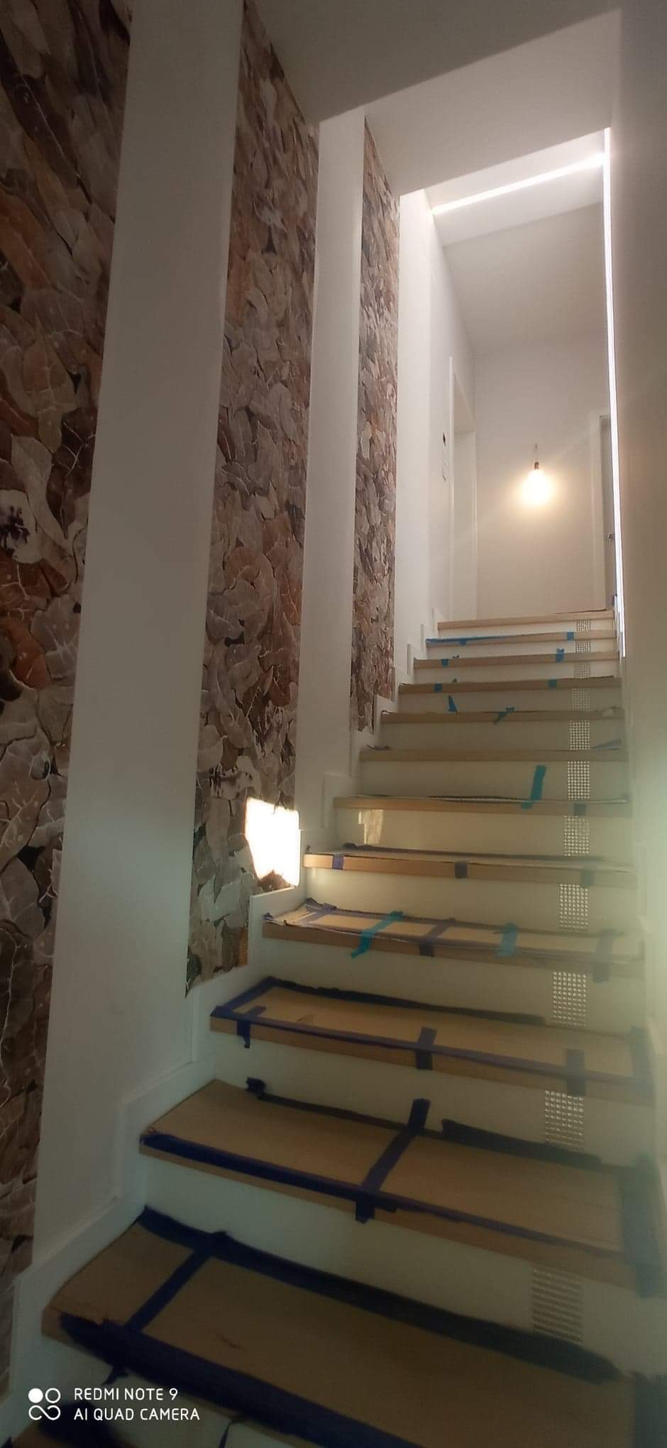 Schody w trakcie zabezpieczania przed remontem, z okładziną kamienną na ścianie i prowizorycznym oświetleniem w korytarzu.