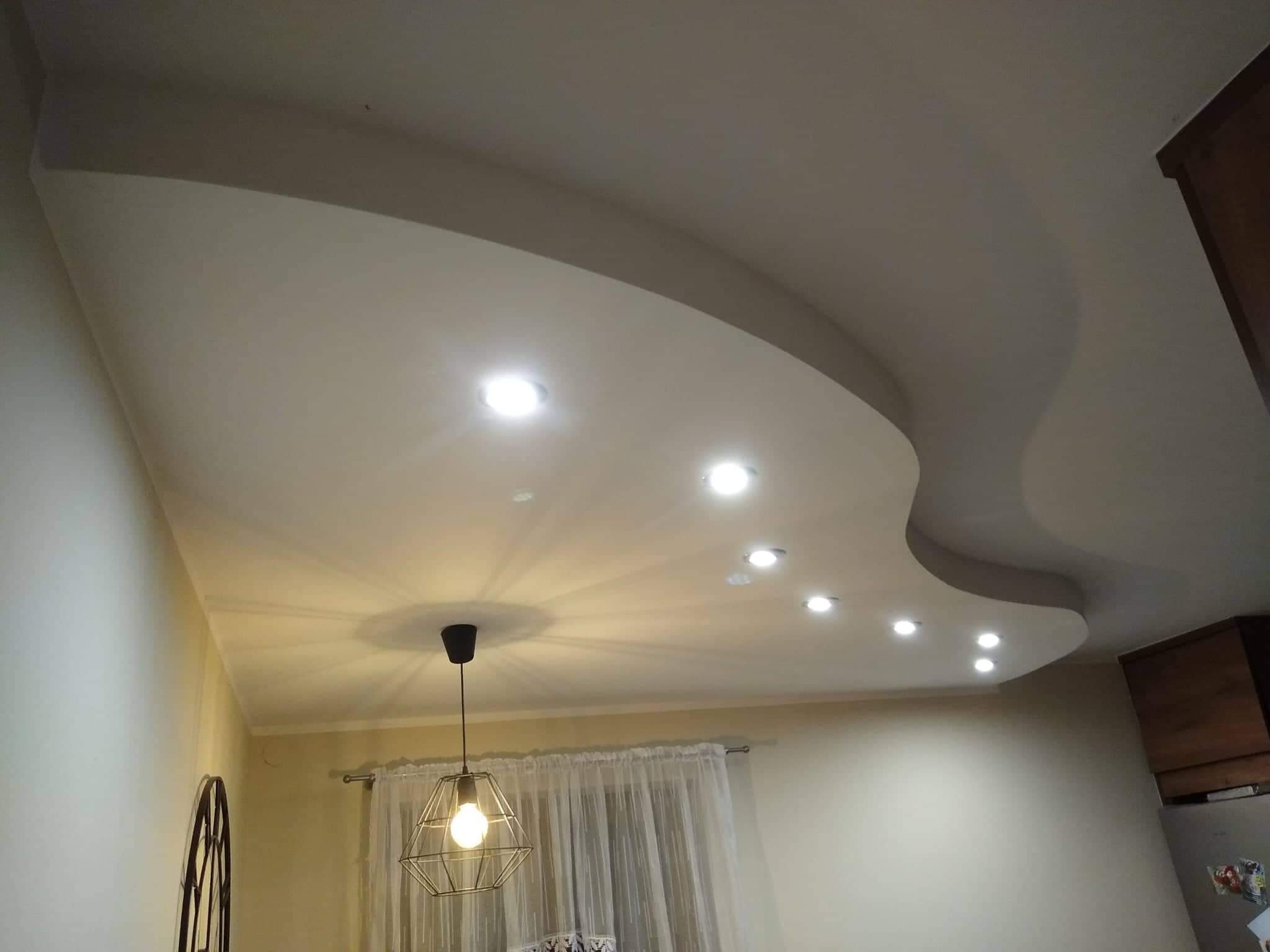 Falisty sufit podwieszany z oświetleniem punktowym i wiszącą lampą w stylu industrialnym, widok z dołu.