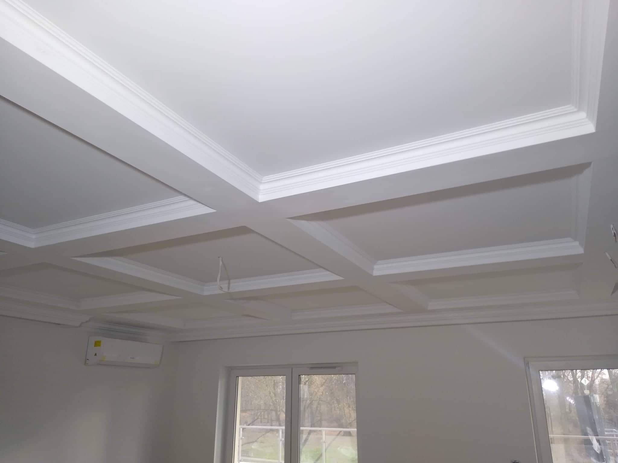 Kasetonowy sufit w jasnym pomieszczeniu z klimatyzacją, widoczne okno z widokiem na drzewa.