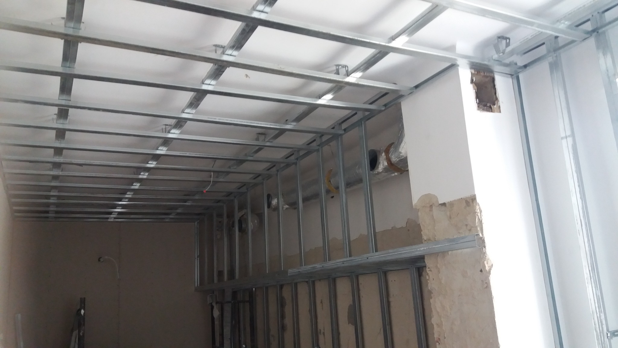 Stelaż metalowy pod zabudowę sufitu i ścian z widocznymi elementami wentylacji w trakcie prac remontowych.