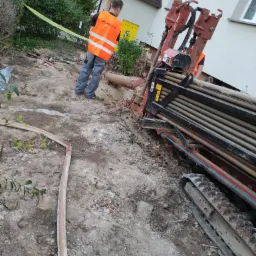 Prace ziemne w Orzeszu: Wiertnica horyzontalna JET TRAC w trakcie wykonywania przewiertu pod instalacje, widoczny pracownik w kamizelce odblaskowej oraz zabezpieczona taśmą strefa robót.