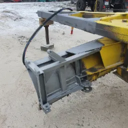 Fragment konstrukcji lawety w trakcie malowania, żółto-szare elementy metalowe, widoczny przewód, na zewnątrz, w tle traktor z przyczepą.