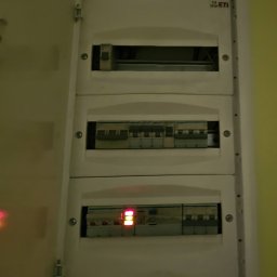 ELEKTROświatło - Otwarta, biała rozdzielnica elektryczna marki ETI, zamontowana na jasnej ścianie, z trzema rzędami modułów zabezpieczających, w tym wyłącznikami z aktywnymi, czerwonymi wskaźnikami.
