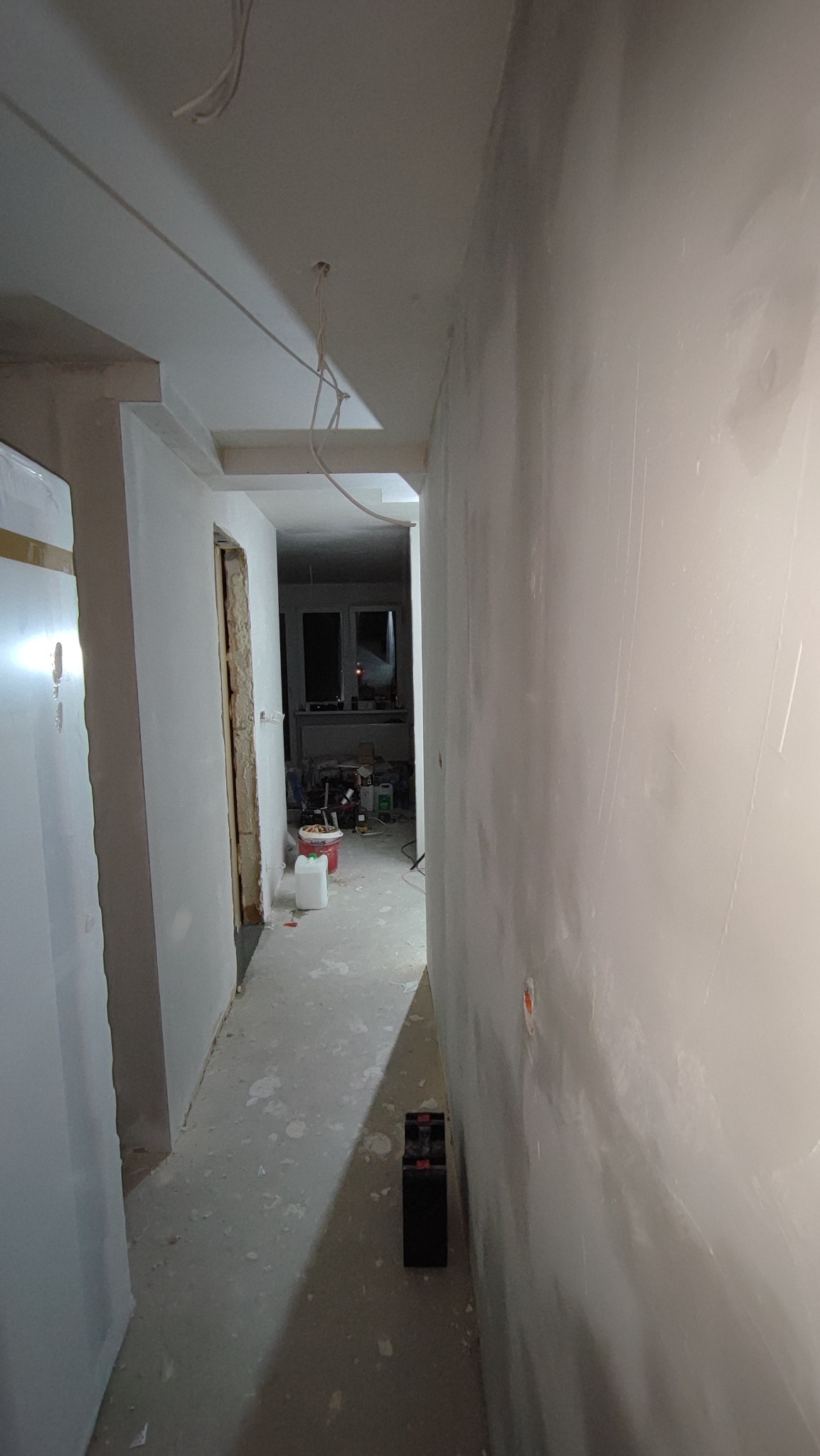 Korytarz w trakcie prac przygotowawczych do malowania, ściany pokryte gładzią, widoczne kable zwisające z sufitu, kubełki z farbą w tle.