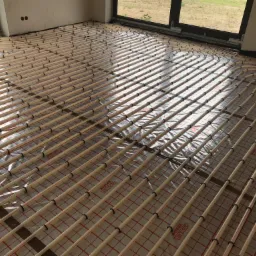 Rozłożona instalacja ogrzewania podłogowego z rurami grzewczymi zamocowanymi do folii z rastrem, widok z góry, pomieszczenie w stanie surowym.