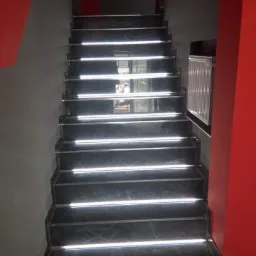 Schody wyłożone czarnym marmurem z podświetleniem LED na każdym stopniu, ściany w kolorze szarym i czerwonym.