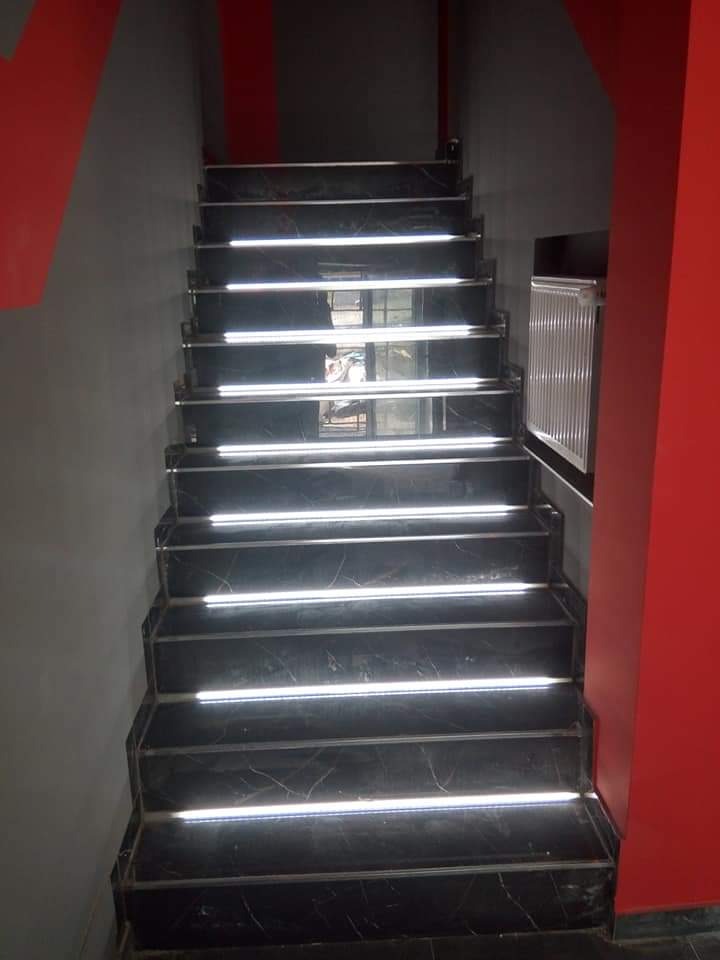 Schody wyłożone czarnym marmurem z podświetleniem LED na każdym stopniu, ściany w kolorze szarym i czerwonym.