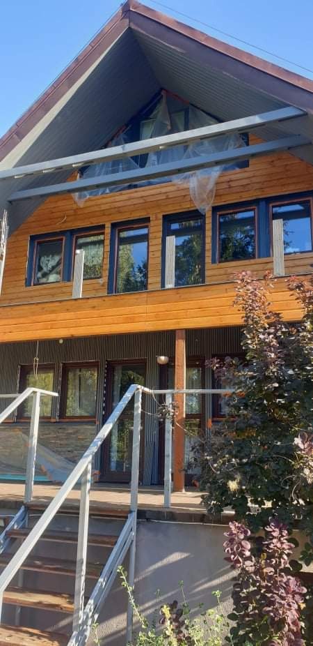 Dwukondygnacyjny dom z drewnianą elewacją w trakcie prac wykończeniowych, zabezpieczony folią ochronną, widoczne rusztowanie i roślina ozdobna.