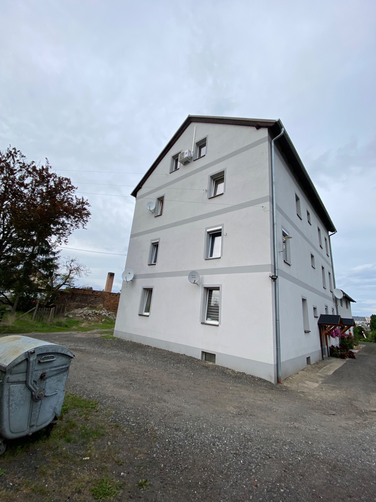 Wielopiętrowy budynek mieszkalny z klimatyzatorami na ścianach zewnętrznych, Czeladź. Widoczny także śmietnik i drzewo.
