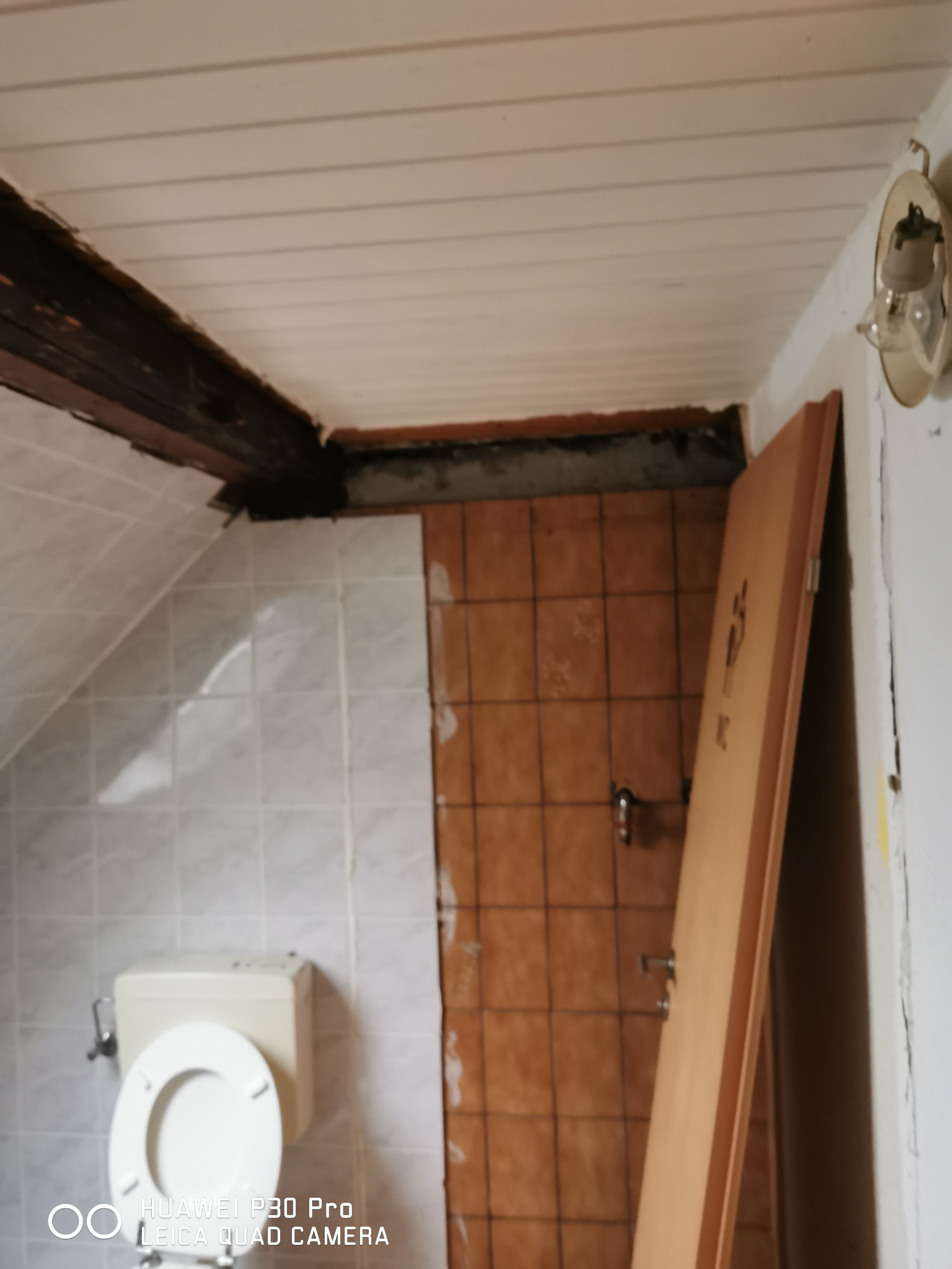 Łazienka w trakcie remontu: widoczne płytki na ścianach, toaleta i niedokończone obramowanie drzwi z częściowo zamontowaną ościeżnicą i skrzydłem drzwiowym z symbolem WC.