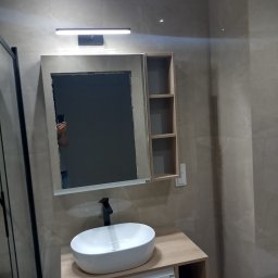Remont Dla Ciebie - Nowoczesna łazienka w beżowych odcieniach z umywalką nablatową, szafką z półkami i lustrem z oświetleniem LED, widoczny fragment kabiny prysznicowej.