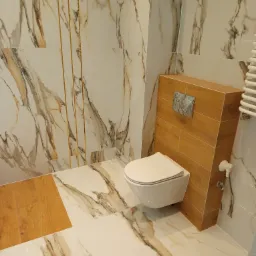 Nowoczesna łazienka z marmurowymi płytkami w odcieniach bieli i brązu, złotymi listwami dekoracyjnymi i podwieszaną toaletą z drewnianą obudową.