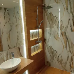 Nowoczesna łazienka z drewnianymi akcentami: umywalka nablatowa, kabina prysznicowa typu walk-in z marmurowymi płytkami i podświetlane wnęki. Designerskie wykończenie.