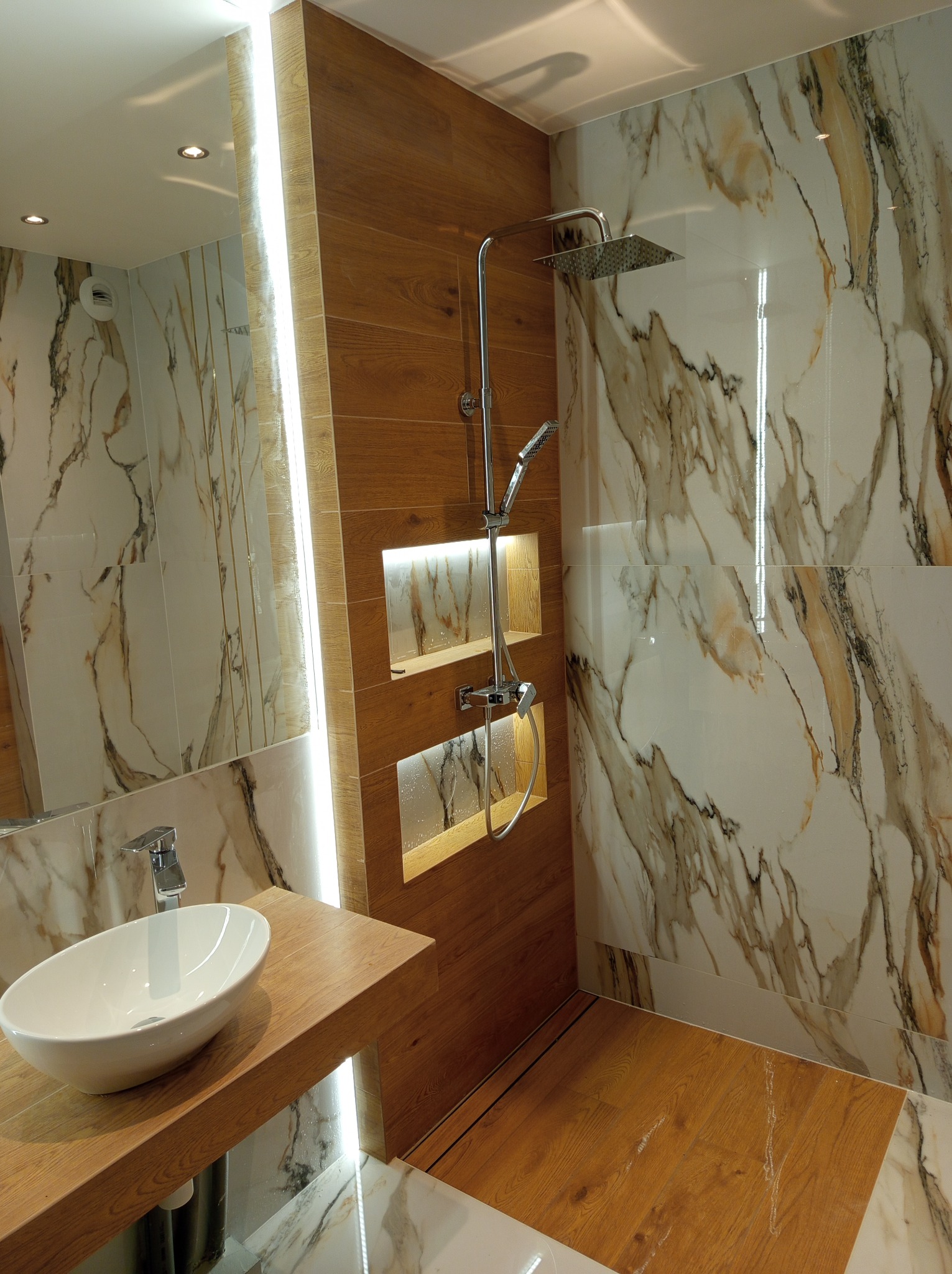 Nowoczesna łazienka z drewnianymi akcentami: umywalka nablatowa, kabina prysznicowa typu walk-in z marmurowymi płytkami i podświetlane wnęki. Designerskie wykończenie.