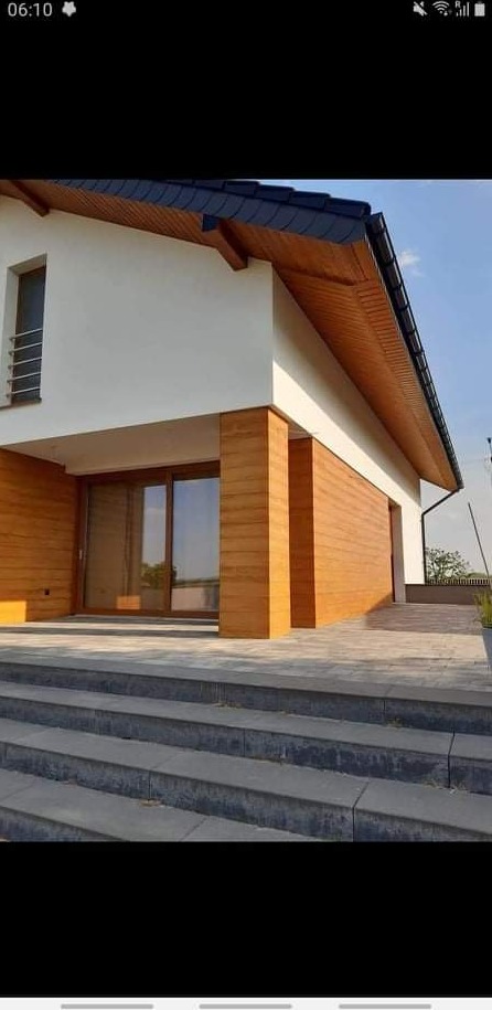 Nowoczesny dom z jasną elewacją i drewnianą okładziną, schody wejściowe z szarej kostki brukowej, widok z dołu.