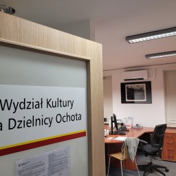 LeoKlima.pl - Wnętrze biura z zainstalowanym klimatyzatorem ściennym, widoczne zza przeszklonych drzwi z napisem 'Wydział Kultury dla Dzielnicy Ochota'.