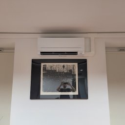 LeoKlima.pl - Biały klimatyzator ścienny zamontowany w pomieszczeniu z obrazem w czarnej ramie poniżej.
