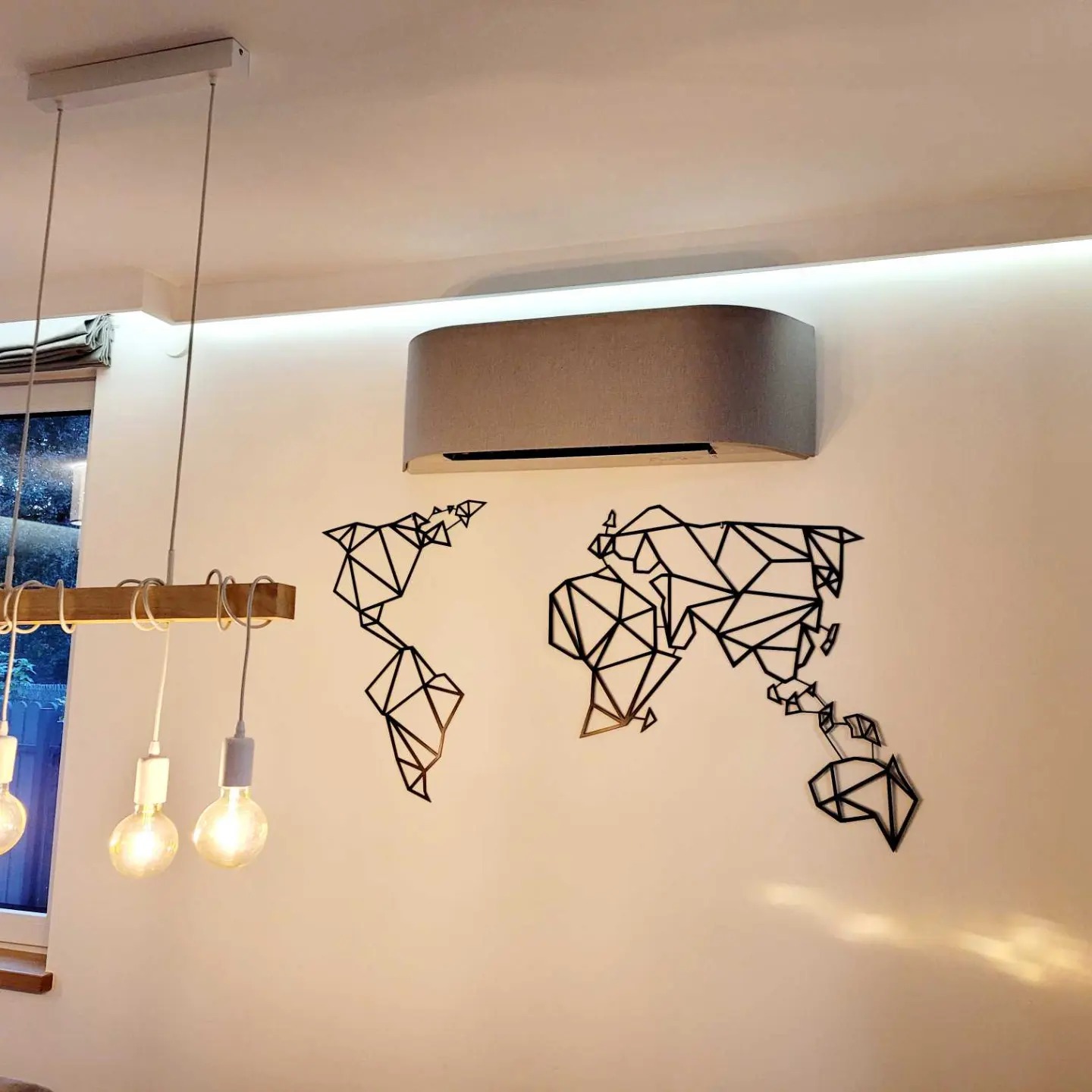 Szary klimatyzator ścienny w nowoczesnym wnętrzu z dekoracją ścienną w postaci geometrycznej mapy świata i wiszącą lampą z trzema żarówkami.