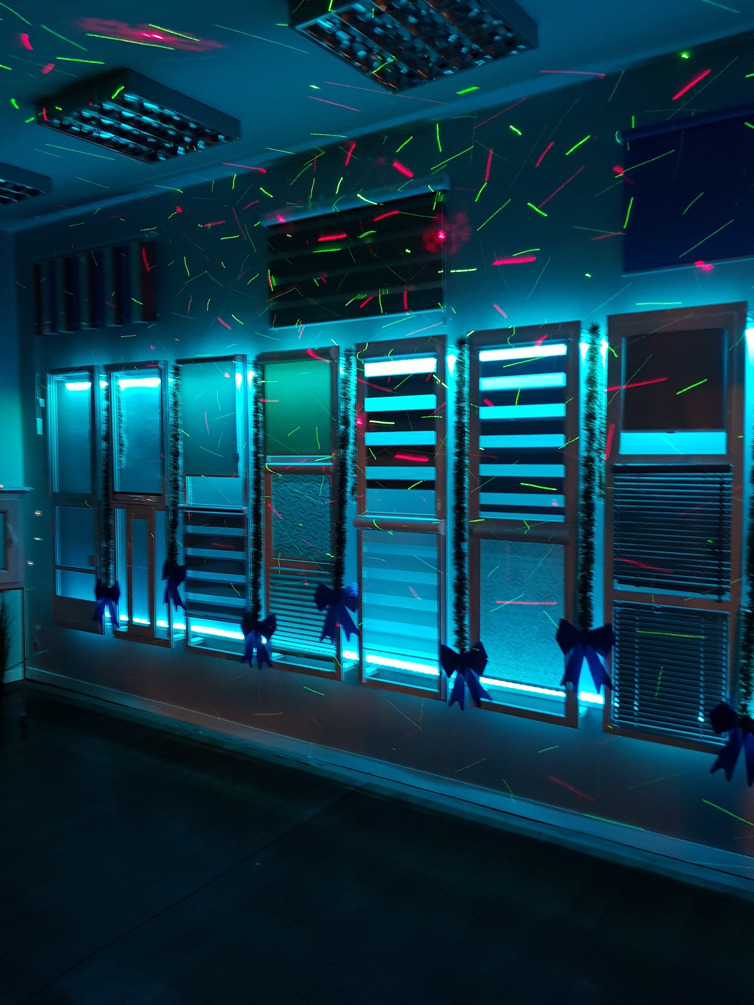 Wystawa różnych typów osłon okiennych w niebieskim oświetleniu dyskotekowym, ozdobione niebieskimi kokardami.