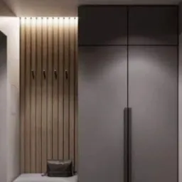 Nowoczesna szafa wnękowa w odcieniach szarości, z drewnianym panelem ściennym z wieszakami i siedziskiem z poduszką, oświetlona punktowo.