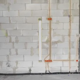 Ściana z betonu komórkowego w trakcie prac instalacyjnych: widoczne bruzdy zalane gipsem z pomarańczowymi puszkami elektrycznymi i przewodami w peszlach ułożonymi wzdłuż podłogi.