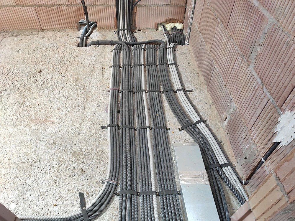 Równolegle ułożone, zabezpieczone peszlami przewody elektryczne, prowadzone wzdłuż surowej ściany z cegły i betonu w trakcie instalacji.