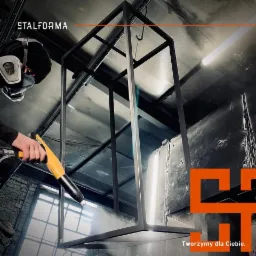 Malowanie proszkowe metalowej konstrukcji w kształcie prostopadłościanu przez pracownika w masce ochronnej. W tle ceglany mur i logo firmy Stalforma.