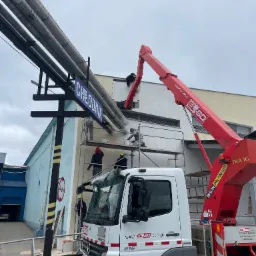 Prace na wysokościach w Choroszczy: pracownicy na rusztowaniu i podnośniku malują elewację budynku przemysłowego z napisem 'CHŁODNIA', widoczne rury i firmowy samochód z podnośnikiem.