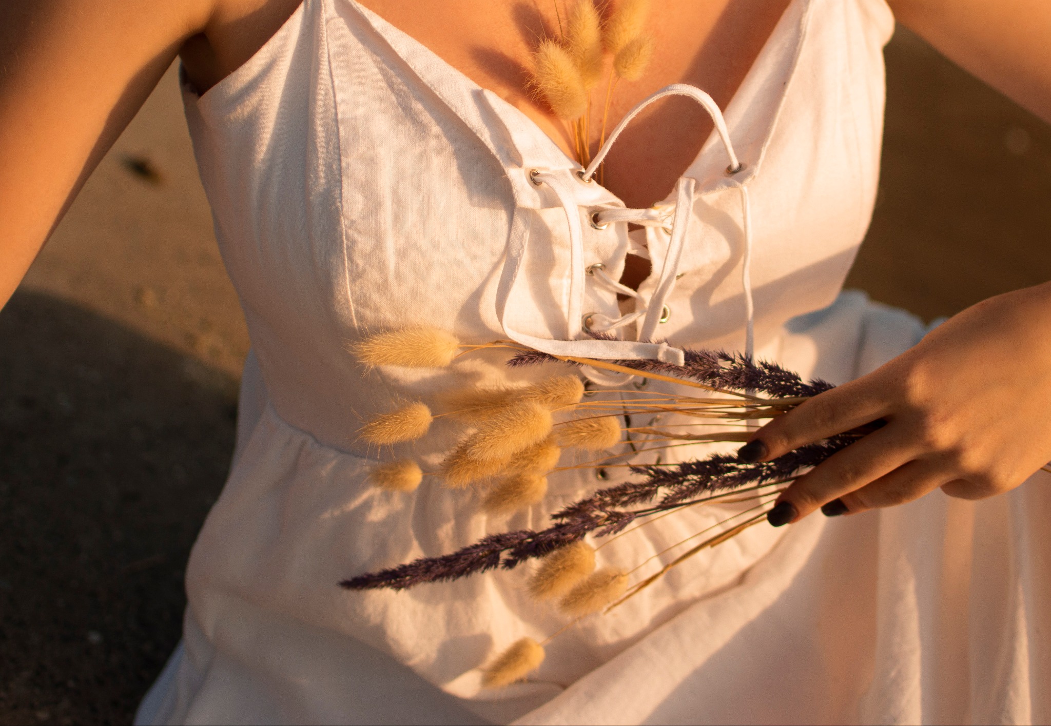 Kobieta w białej sukience trzyma bukiet suszonych traw w ciepłym, naturalnym świetle.