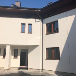 Olbud - Nowoczesny budynek dwukondygnacyjny z jasną elewacją, brązowymi ramami okiennymi i drzwiami, widoczne elementy wykończeniowe, jeszcze bez drzwi wejściowych.