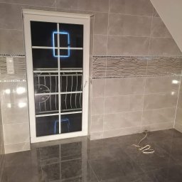 Nabłysk - Wykończona łazienka na poddaszu z szarymi płytkami imitującymi marmur na ścianach i podłodze, białe okno z kratką i dekoracyjny pas płytek na ścianie