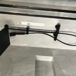 Czarny, nowoczesny zestaw prysznicowy z deszczownicą i słuchawką, zamontowany w kabinie z szarymi płytkami imitującymi marmur.