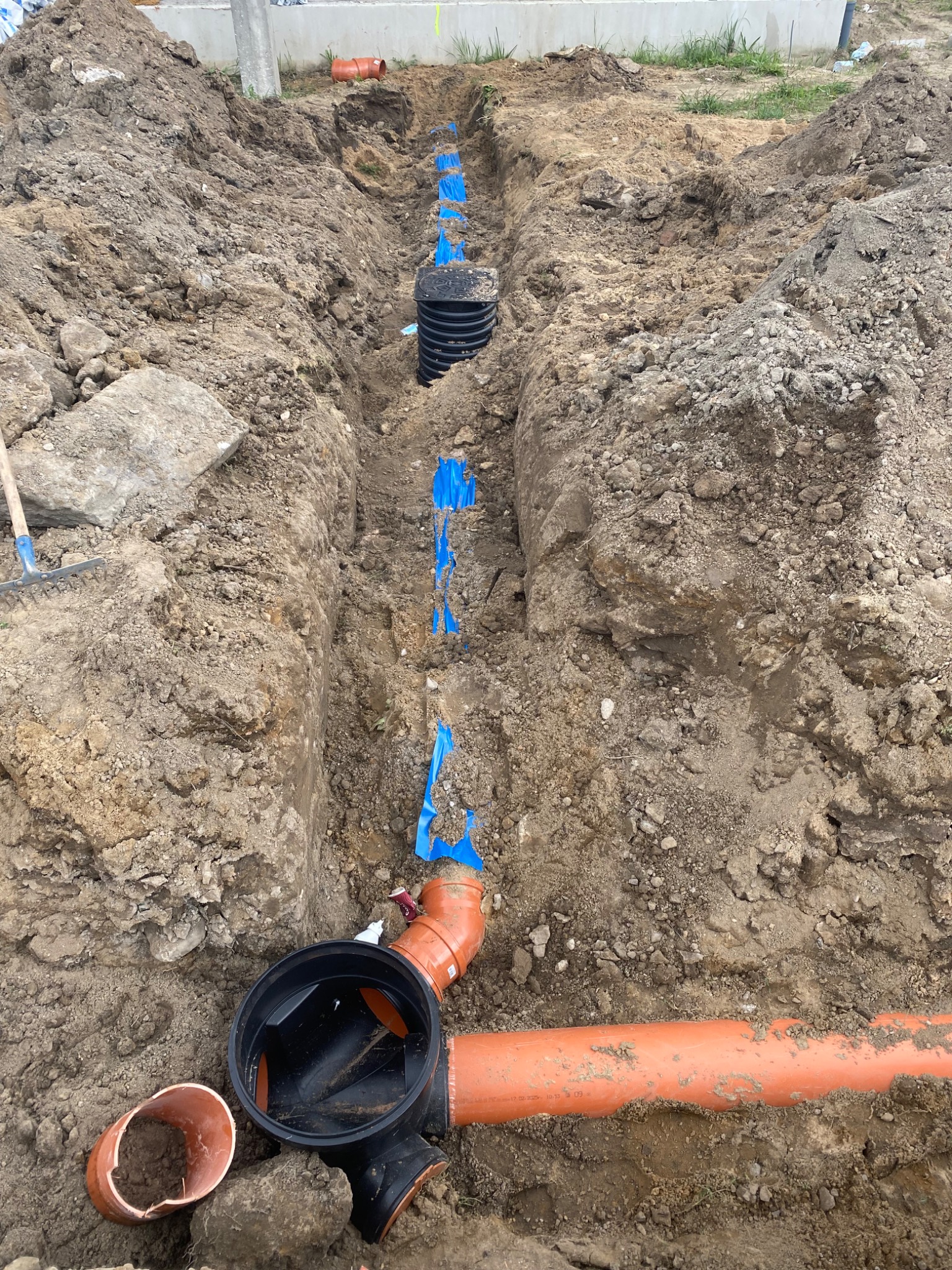 Wykop z ułożonymi rurami kanalizacyjnymi w Rypinie. Widoczne elementy instalacji i wykopana ziemia. Ujęcie z góry, prezentujące etap prac ziemnych.