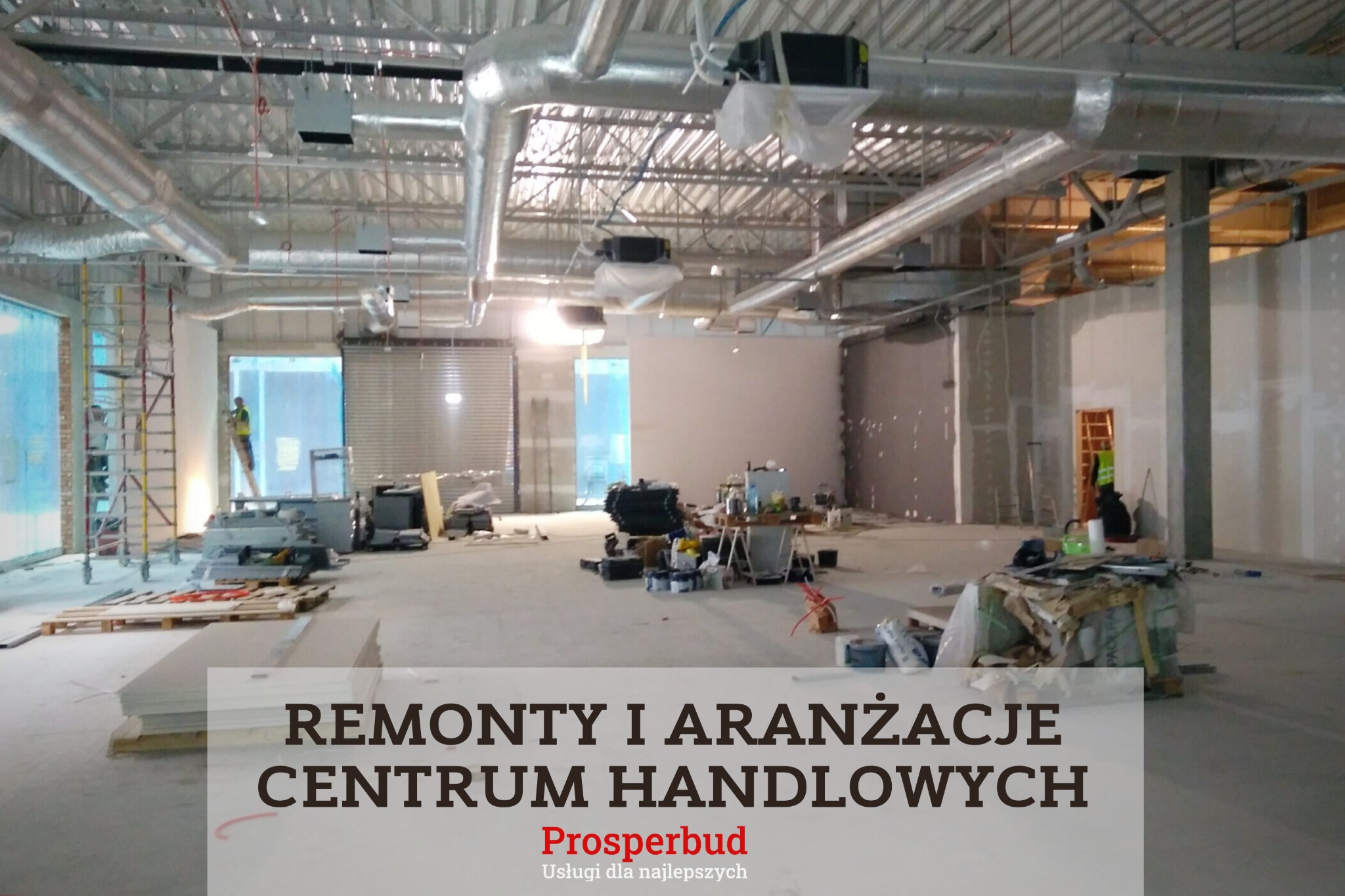 Wnętrze w trakcie prac wykończeniowych w obiekcie handlowym, widoczne surowe ściany, instalacje pod sufitem, materiały budowlane i pracownik na drabinie.