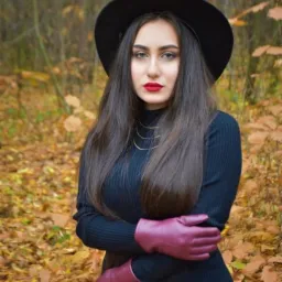 Portret kobiety w czarnym kapeluszu i bordowych rękawiczkach na tle jesiennego lasu.