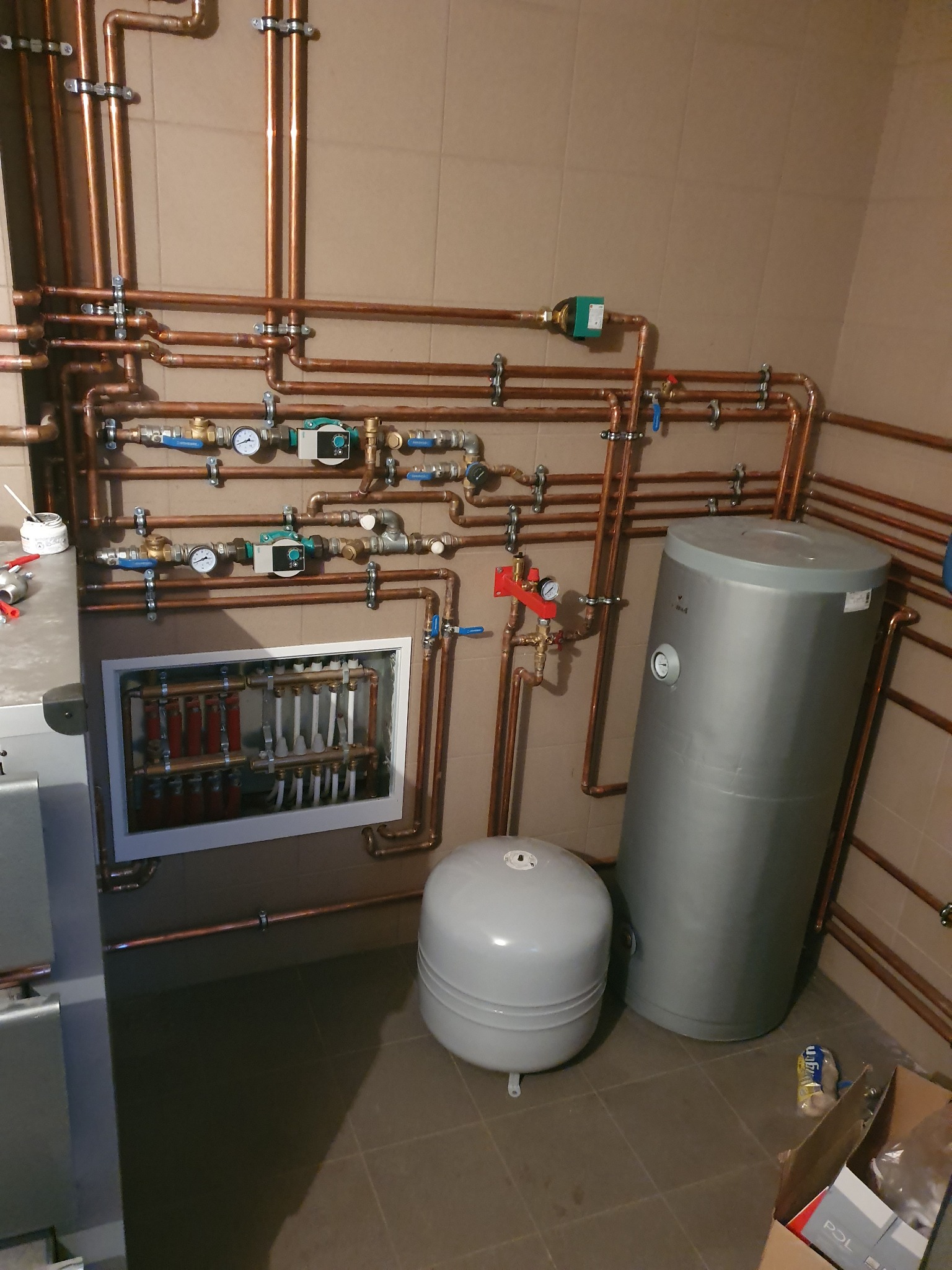 Złożona instalacja centralnego ogrzewania z miedzianych rur, rozdzielacz podłogowy w obudowie, zbiornik akumulacyjny i naczynie przeponowe w kotłowni we Władysławowie.