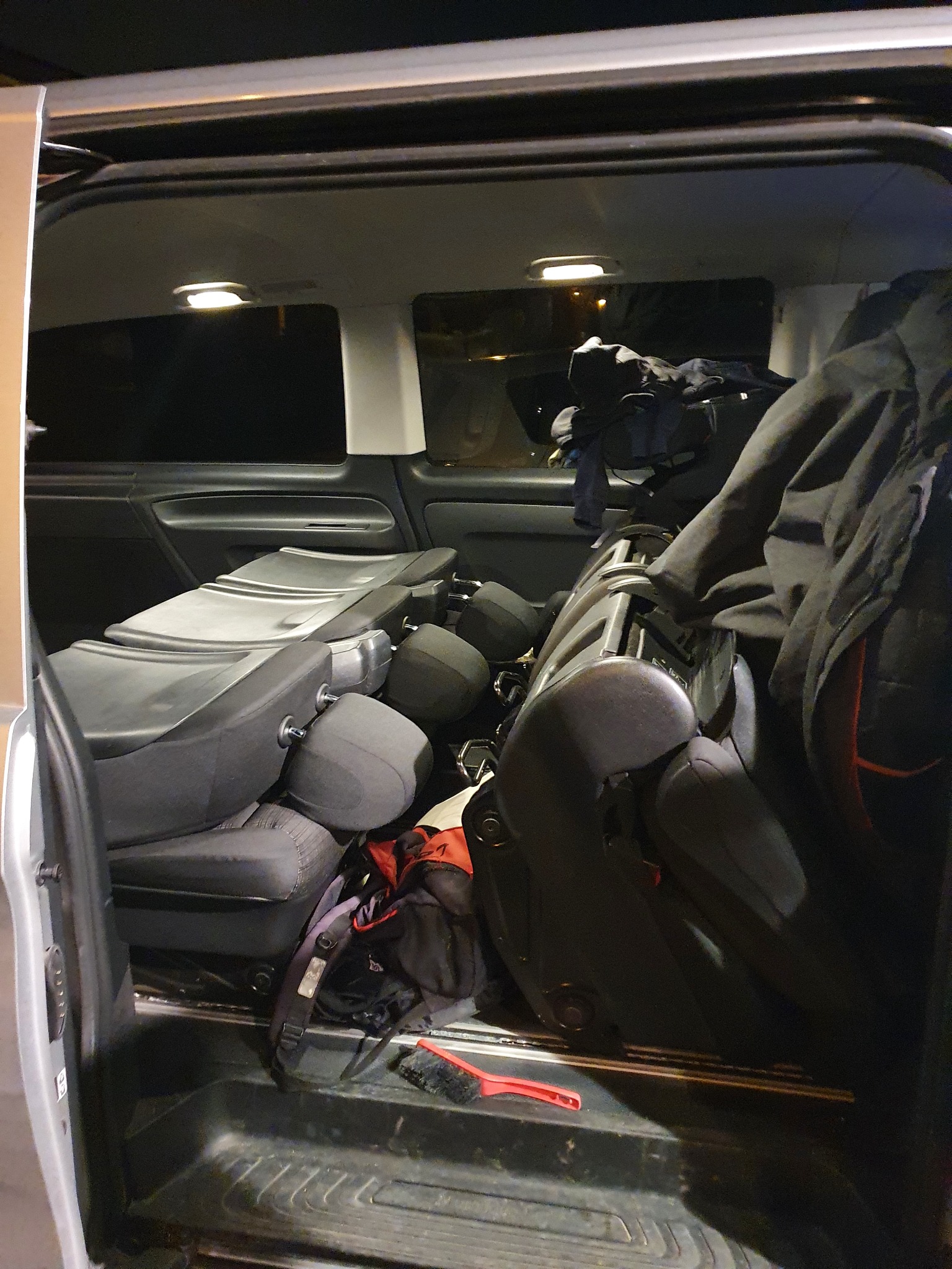 Wnętrze busa z wyjętymi siedzeniami pasażerskimi, widoczny plecak, kurtka i czerwona szczotka do zamiatania.