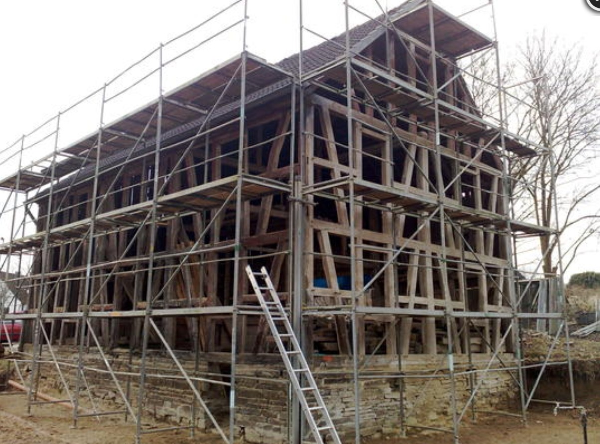 Dom w konstrukcji szkieletowej, otoczony rusztowaniem, widoczna drabina oparta o rusztowanie, odsłonięte fundamenty.