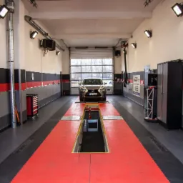 Samoch&oacute;d Lexus na stanowisku diagnostycznym z kanałem w warsztacie samochodowym, widok z przodu, oświetlenie sufitowe