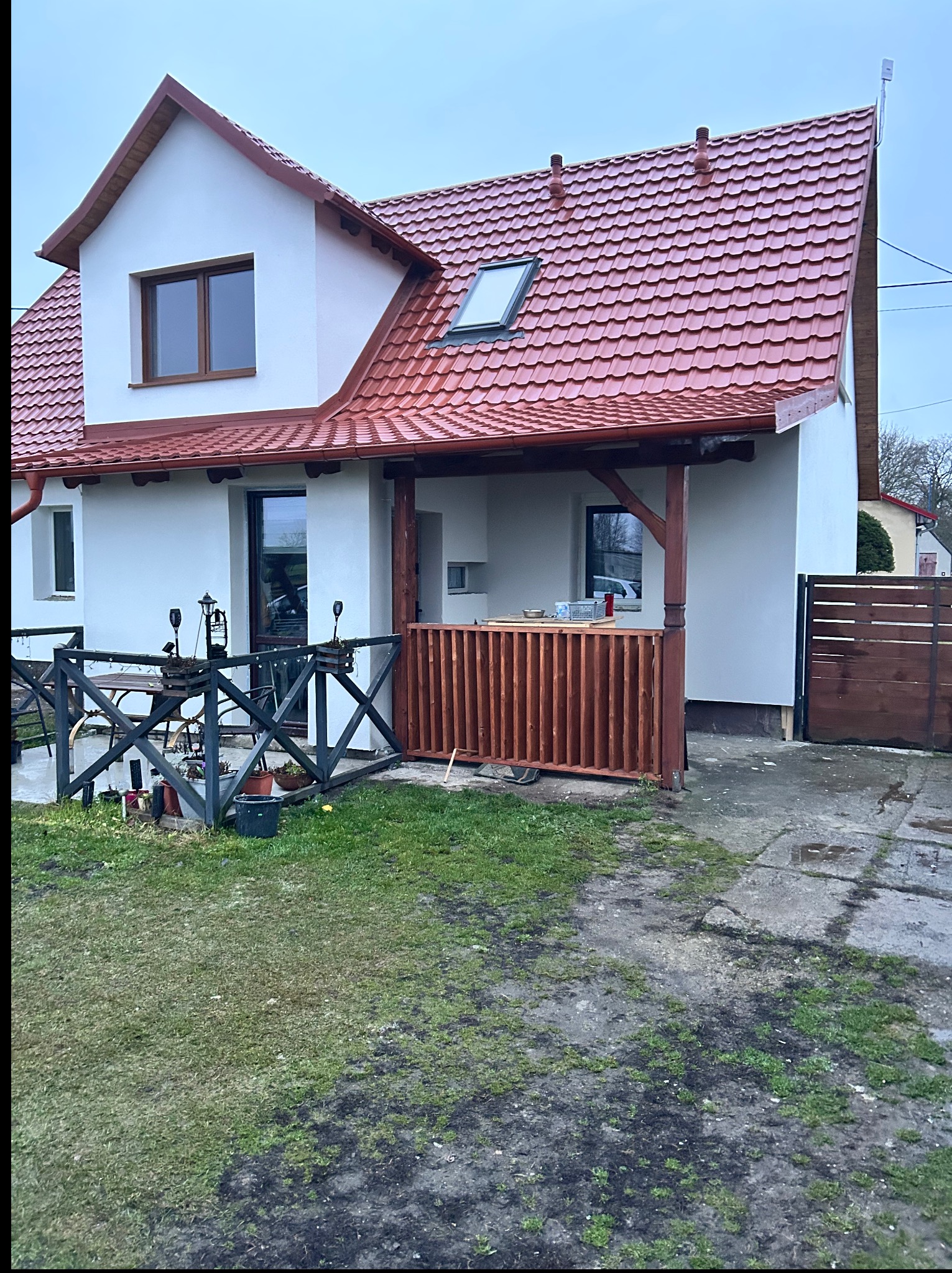 Biały dom z czerwoną dachówką po remoncie, widok z zewnątrz. Nowe okna, odnowiona elewacja i drewniane elementy wykończeniowe.