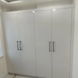 Biała, czterodrzwiowa szafa wnękowa z czarnymi, minimalistycznymi uchwytami, dopasowana do wnętrza z marmurową podłogą.