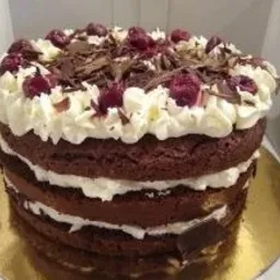 Tort Szwarcwaldzki z bitą śmietaną, wiśniami i startą czekoladą, widoczny na złotym podkładzie.