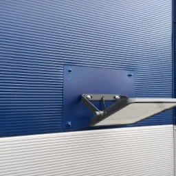 Szary reflektor LED zamontowany na niebieskiej, żebrowanej ścianie budynku w Krempachach, widoczny fragment białej ściany poniżej.