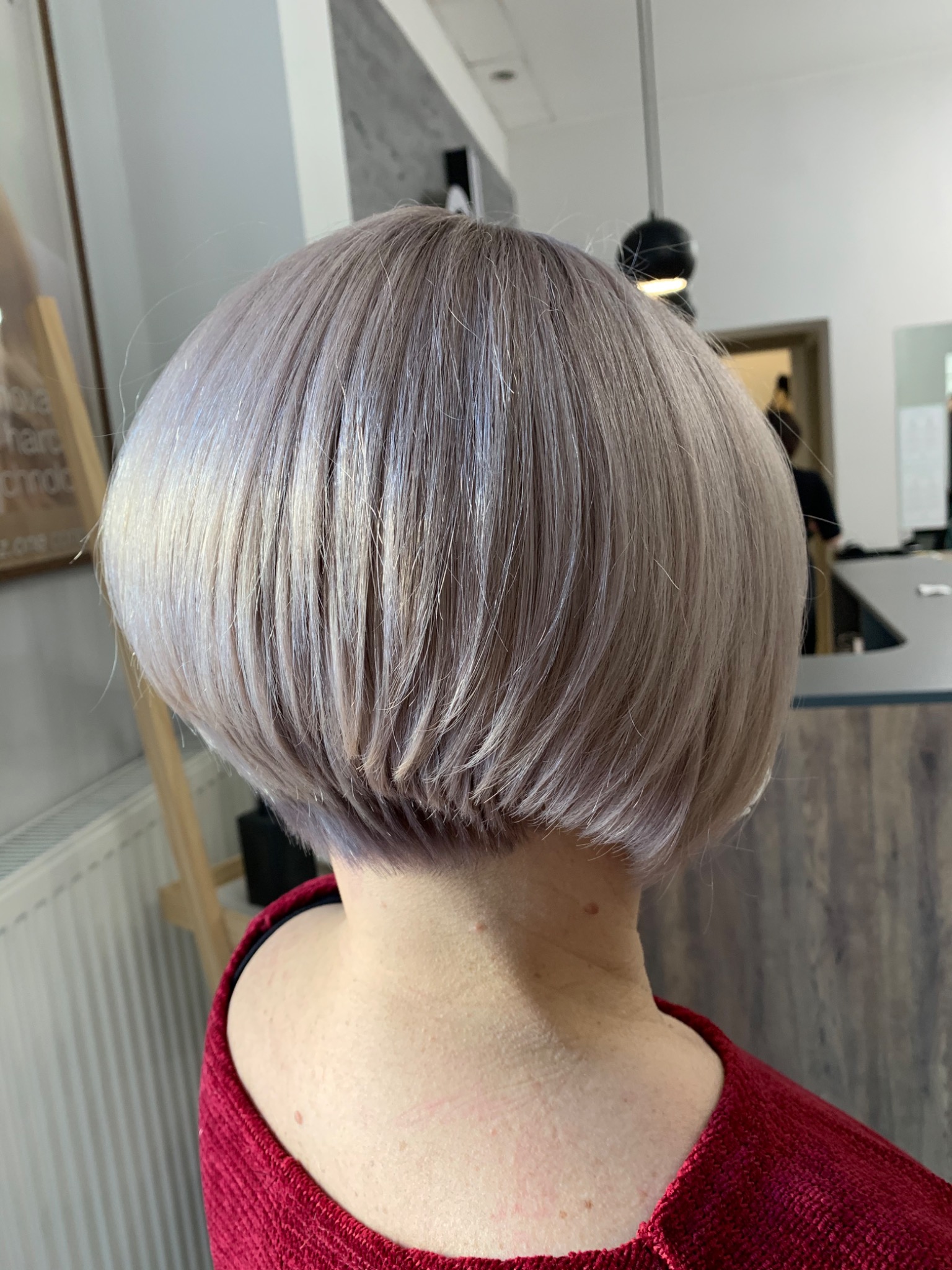 Krótka, popielata fryzura bob z widocznym podcieniowaniem na karku, sfotografowana z tyłu w salonie fryzjerskim.