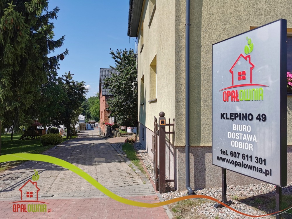Tablica informacyjna firmy Opałownia z adresem Klepino 49, informacjami o biurze, dostawie i odbiorze, numerem telefonu i adresem strony internetowej, umieszczona przed budynkiem firmy i brukowaną...