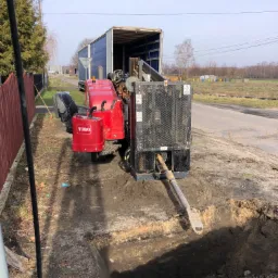 Koparka Toro w trakcie wykonywania wykopu pod instalacje, widoczny wykop w ziemi i ciężarówka w tle.