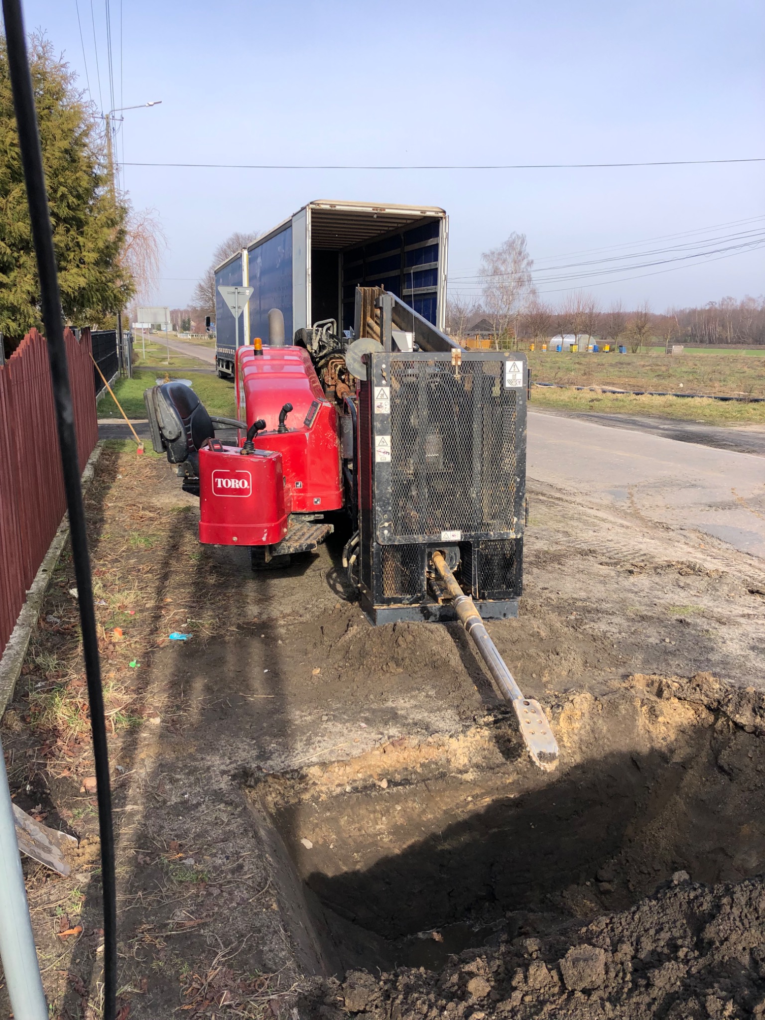 Koparka Toro w trakcie wykonywania wykopu pod instalacje, widoczny wykop w ziemi i ciężarówka w tle.