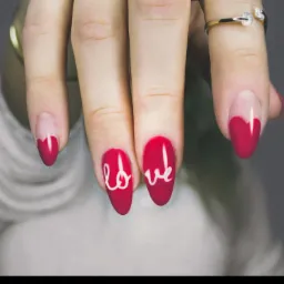 Dłoń z czerwonym manicure, na dwóch paznokciach biały napis LOVE, na serdecznym palcu pierścionek z cyrkoniami.