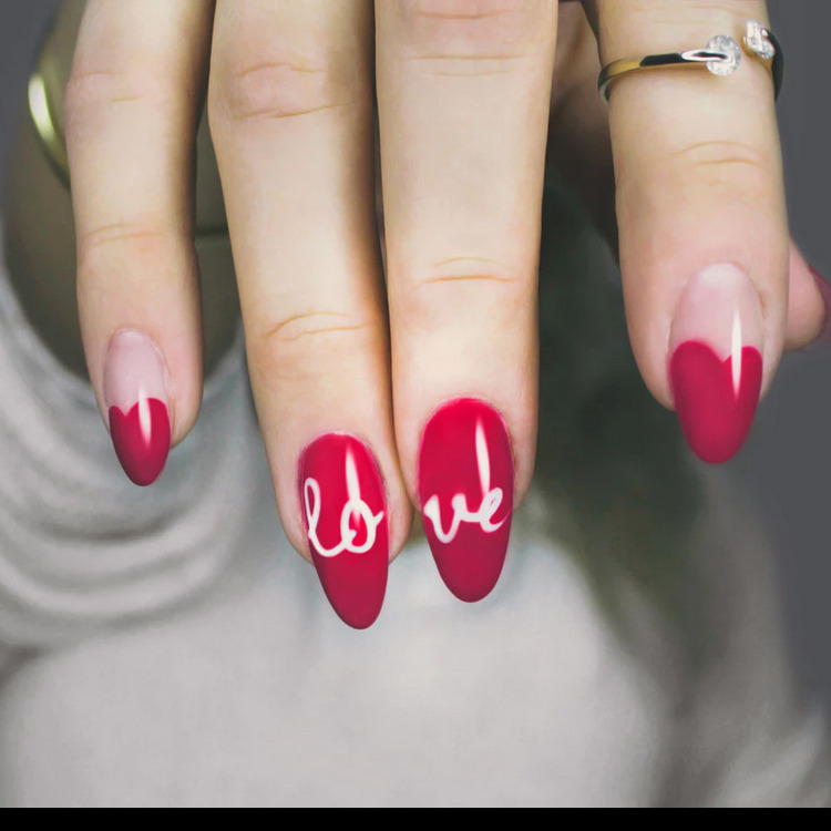 Dłoń z czerwonym manicure, na dwóch paznokciach biały napis LOVE, na serdecznym palcu pierścionek z cyrkoniami.
