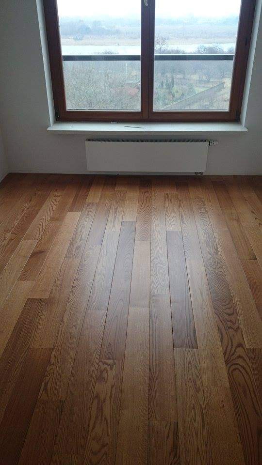 Wykończona podłoga z parkietu dębowego w pokoju z oknem dachowym i grzejnikiem pod oknem. Widoczna faktura drewna i lakierowana powierzchnia.